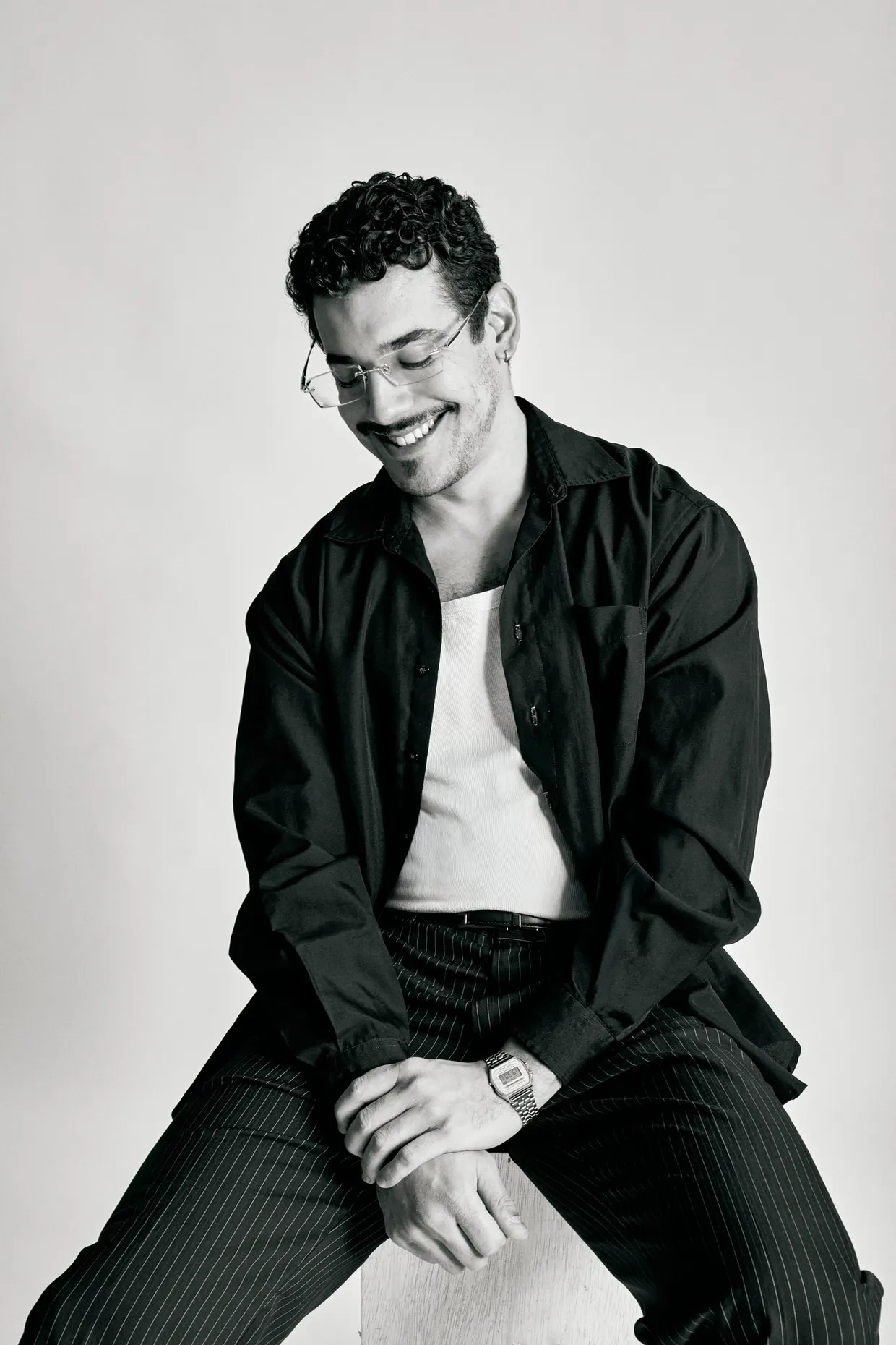 Retrato em preto e branco de homem sentado, sorrindo com o olhar voltado para baixo.